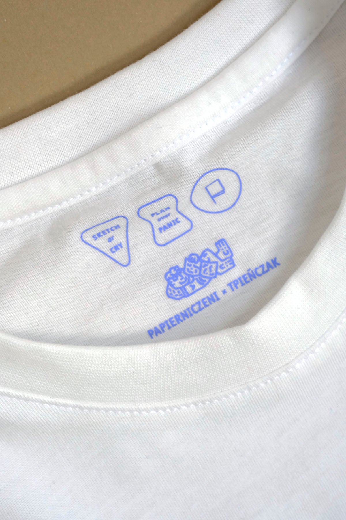 Zbliżenie na niebieskie detale Papierniczeni x TPieñczak na białym T-shircie.