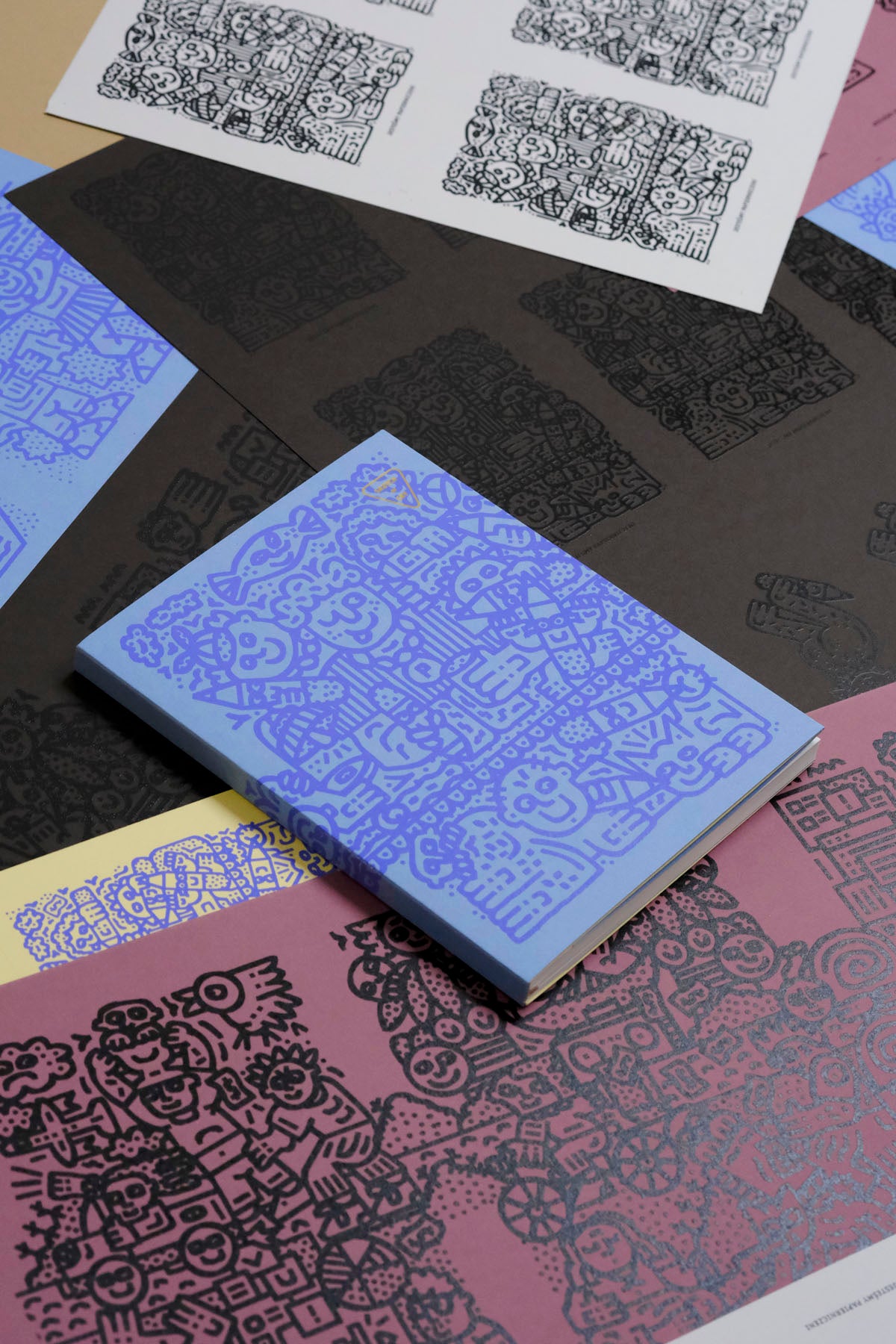 Niebieski szkicownik z fioletową grafiką na tle okładek z grafiką TPieñczaka.